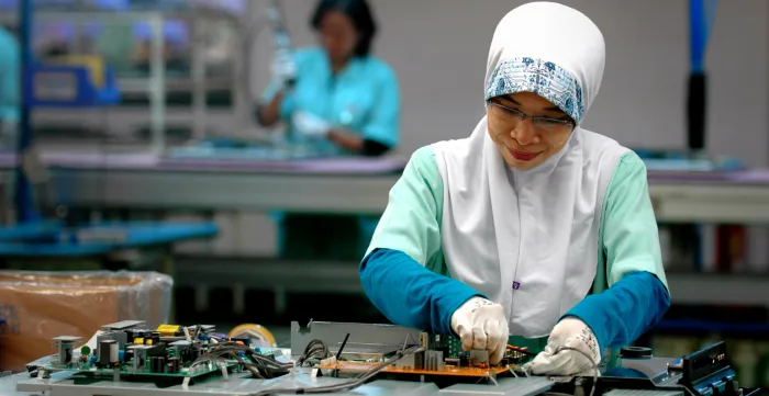A woman electronics worker in Indonesia stands at her work station.