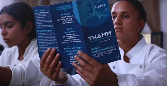 Two women in white shirts, one holds up THAMM brochure