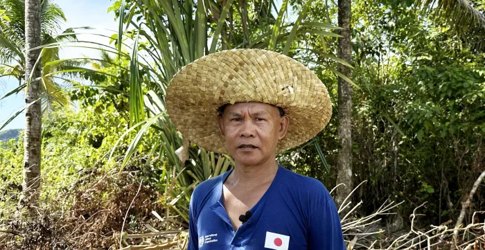 Rolly wearing a buri native hat next to a coconut tree.