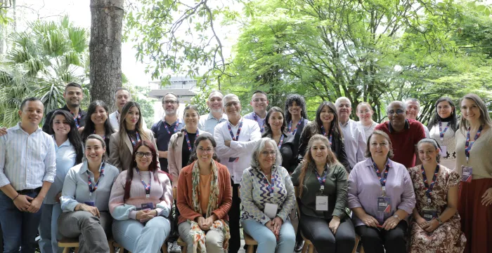 Group photo of the programme’s participants – more than 20 people smiling while posing in a green outdoor area.