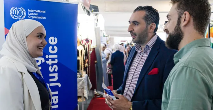 A woman speaking to two men at a garment exhibition in Syria