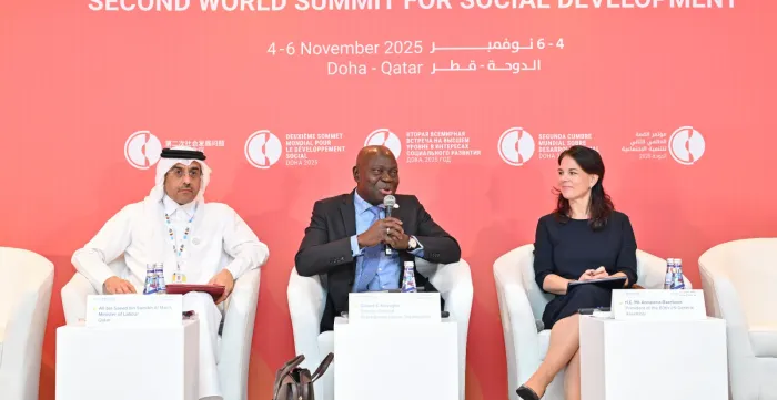 Three people sat on white chairs in formal discussion talking, two men and one woman
