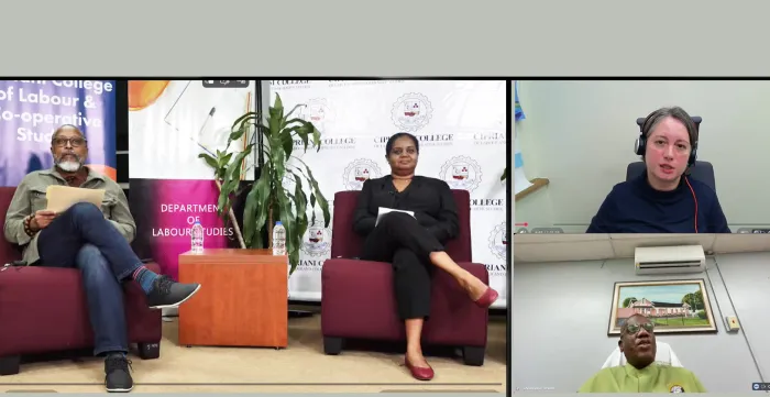 Screenshot of a webinar shows two people seated in armchairs on a studio set on the left, with banners and a potted plant behind them, and two additional speakers joining remotely in smaller video windows on the right. 