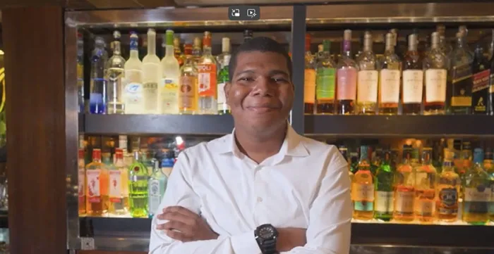 A young employee stands behind the bar counter, smiling