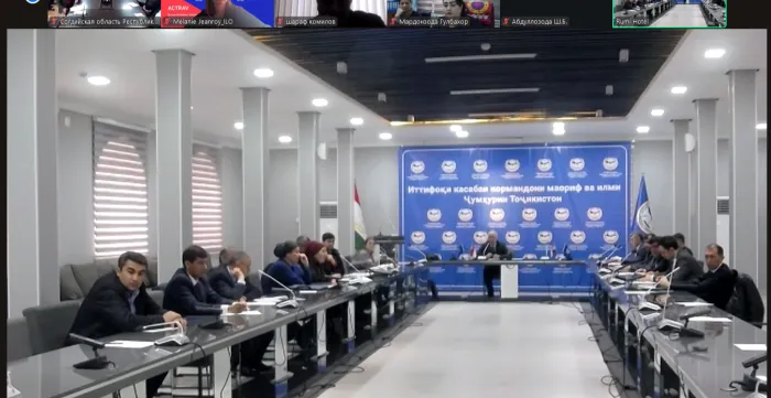 People seated around a long conference table in a meeting room with microphones and a blue backdrop.