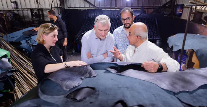Four individuals are standing around a pile of leather pieces as they have a conversation.