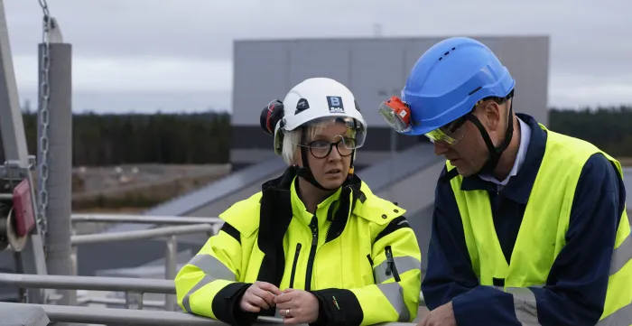 Two workers wearing helmets and yellow vests standing next to each other.