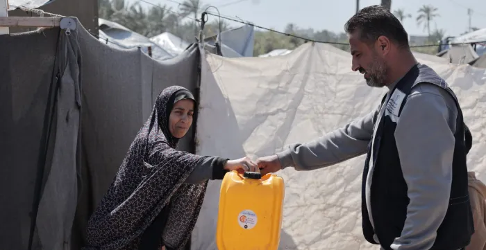 A man hands an empty oil can to a woman refugee to use as safe water container.