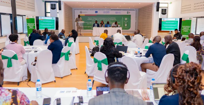 Participants seated around conference tables listen to presentations and discussions during a regional workshop on migration data management and governance in a meeting hall.