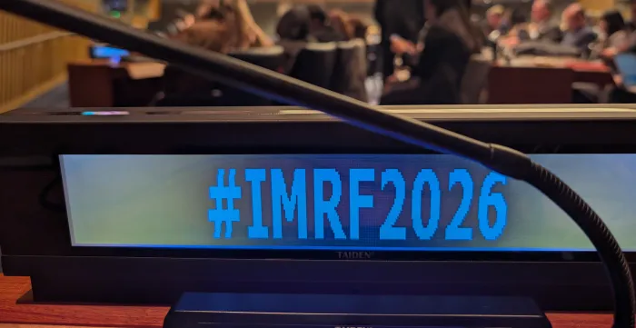 View of a screen in a conference room displaying the conference hashtag #IMRF2026