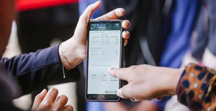 Two people review information on a smartphone displaying a dairy cooperative management application. One person points to production and payment data on the screen, illustrating the use of digital tools to improve record-keeping, transparency, and financial access for dairy farmers.