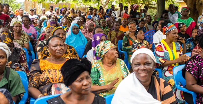 A large group of women, men and young people participate in a community sensitization session focused on health insurance, social protection and child labour prevention.