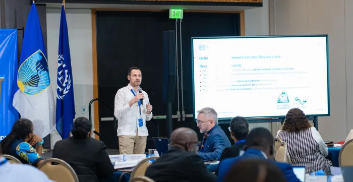 A male presenter speaking into a microphone during a conference presentation at a Hyatt Regency venue.