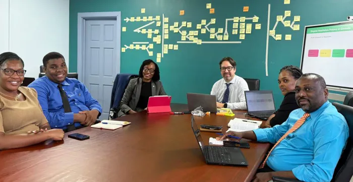 A group of six professionals sits around a large wooden conference table in a meeting room.