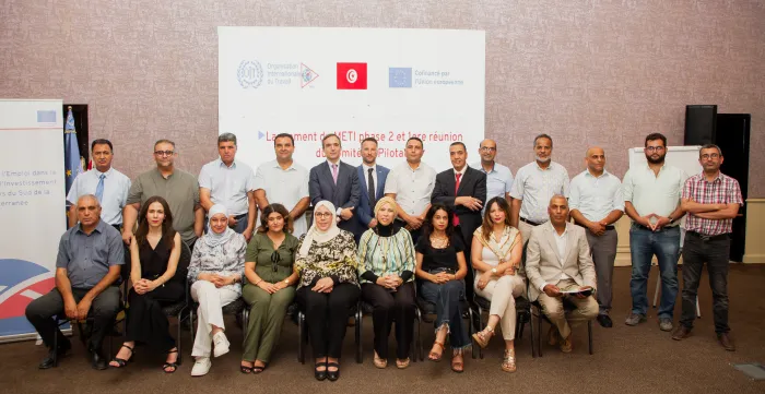 Photo de groupe des participants au lancement de la deuxième phase du programme METI en Tunisie et à la première réunion du comité de pilotage. Les participants posent devant un écran affichant le titre de l’événement ainsi que les logos des partenaires.