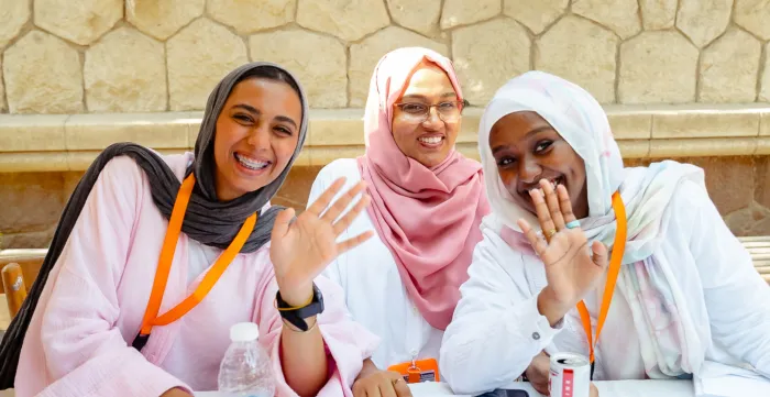 Three women seated at a table laugh to the camera.