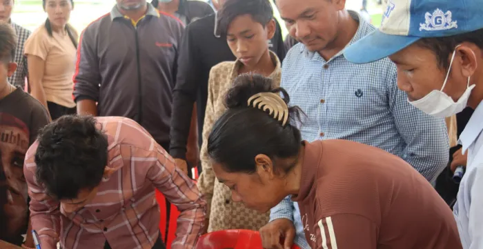 People completing documents while others stand and observe. 