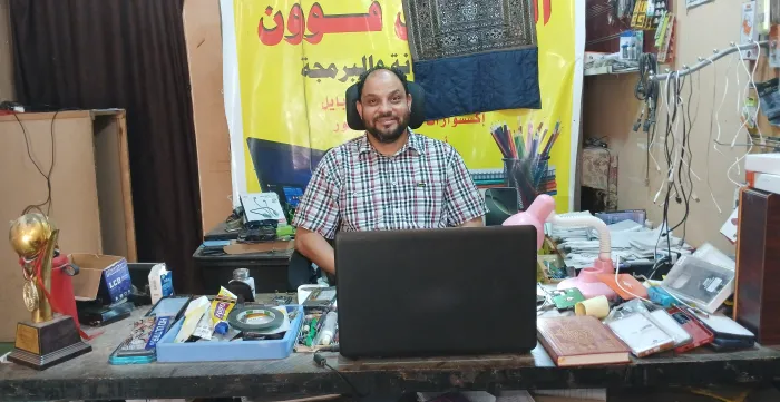 Alhassan Ali sits behind a desk in his mobile phone repair shop. 