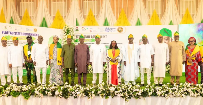 A group of government officials, ILO representatives and other stakeholders stand together on a decorated stage