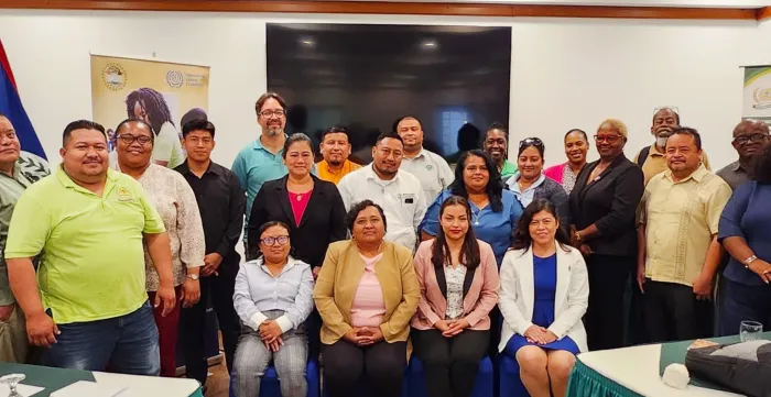 A group photograph of approximately 20 professionals attending a labour complaints tribunal event in Belize. The diverse group of men and women are dressed in professional and business casual attire, smiling at the camera.