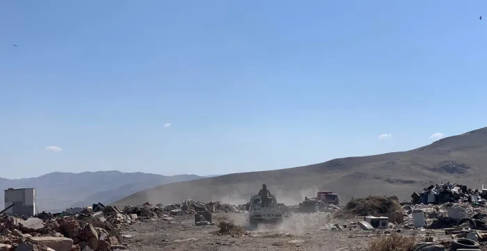 A vehicle drives through a dusty landfill