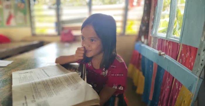 An elementary school girl smiling and reading her book.