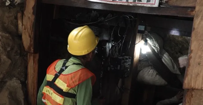 A miner wearing a hard hat and protective gear enters a mining tunnel during a safety inspection.