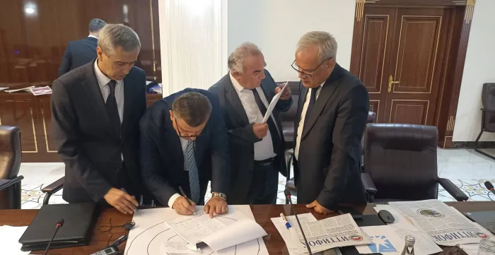 Four men work together over papers and a diagram on a conference table