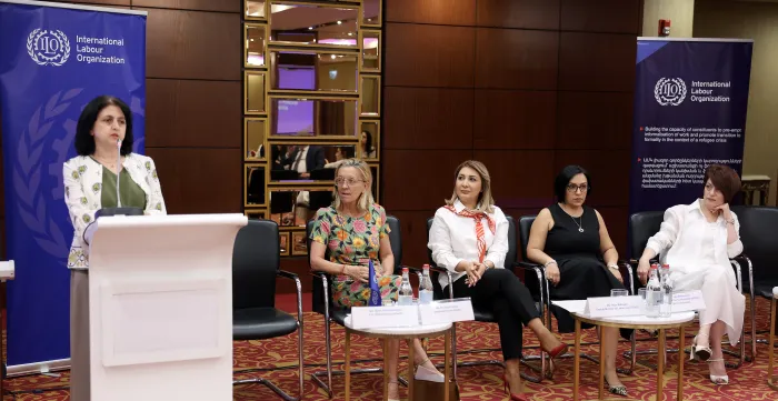A woman speaking at a podium and four panellists seated beside her