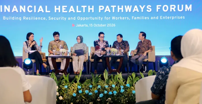 Six panelists seated on stage during the Financial Health Pathways Forum. The moderator at the left speaks into a microphone while the other panelists listen and interact, with audience members visible in the foreground.