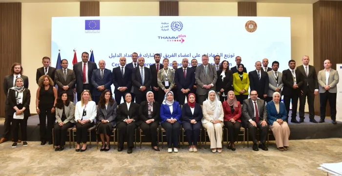 Group photo of men and women standing in several rows on stage in front of a screen.