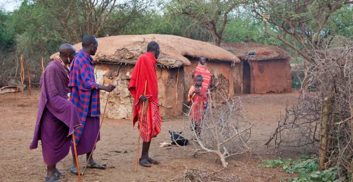 Maasai men leave the homestead as they speak with a woman who remains behind with a child, reflecting gendered patterns of mobility and care responsibilities in pastoral communities in Kenya