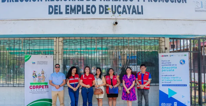 Siete personas posan frente a un edificio, entre dos banners institucionales colocados a ambos lados del grupo.