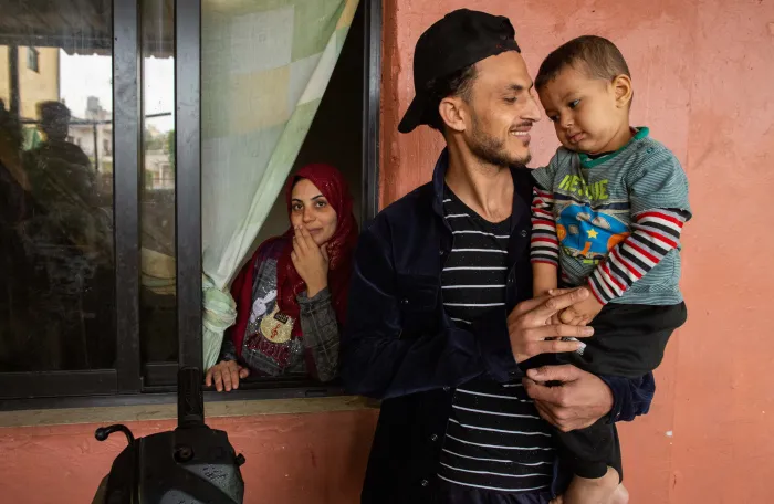 A father holding son in his arms and mother standing in the background