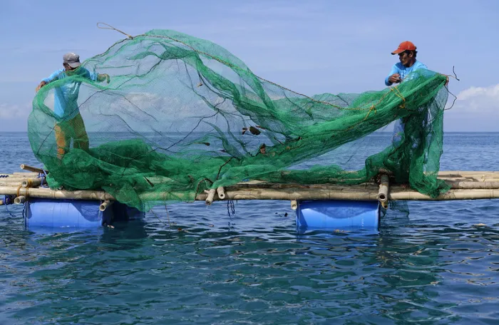 Fishers folding a green fishing net next on a handmade boat