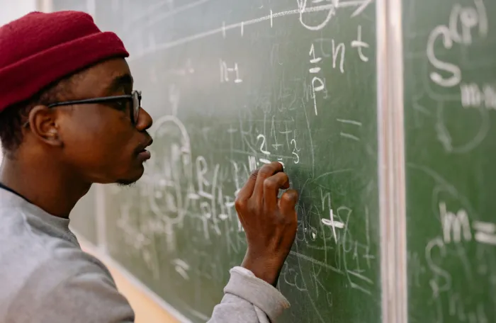 A young man is writing calculations on a black board