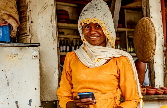 A woman standing in front of a fruit stand holding a cell phone