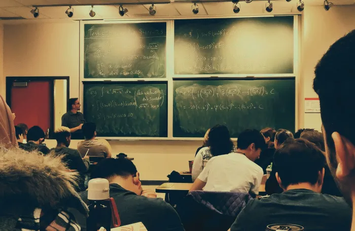 Seated students in a university classroom, teacher next to big illuminated blackboard