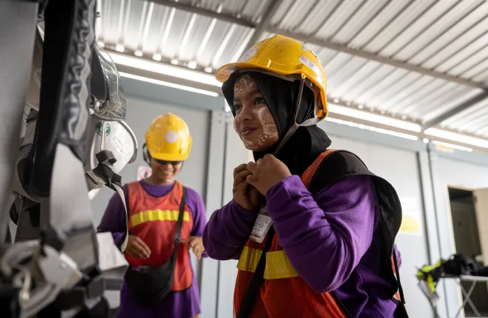 Two women workers in hard hats and safety vests at a worksite in Myanmar.