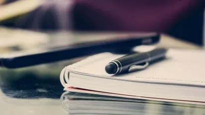 Photo of a notepad with a pen placed on top of it.