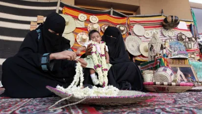 A Saudi woman threads fresh flowers together to sell in a souk
