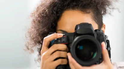 A young African lady holds a professional camera to take a picture 