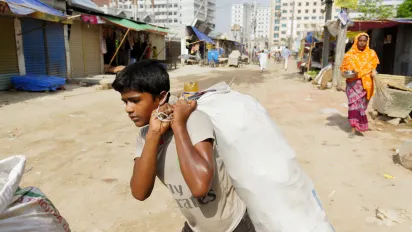 A child carries a bag across an unpaved road on the outskirts of the capital Dhaka, Bangladesh.