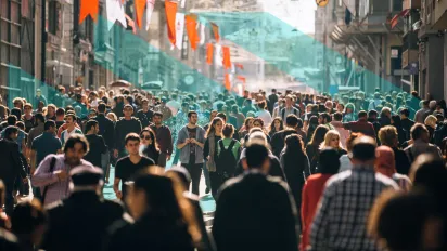 A large crowd of people walking along a busy pedestrian street decorated with red-and-white flags.