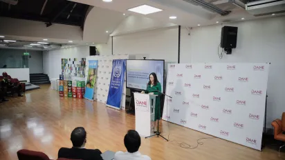 Presentadora del evento en el podio frente al auditorio. A su alrededor, banners del DANE OIT y Unicef. En el fondo, hay cubos con los Objetivos de Desarrollo Sostenible (ODS) de las Naciones Unidas.