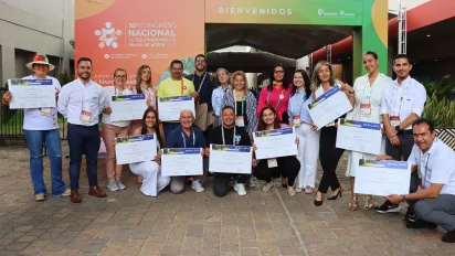 Foto grupal de los mejores estudiantes del diplomado Palma sostenible: Programa de formación para el trabajo decente en frente de un stand en el Congreso Palmero sosteniendo sus certificaciones