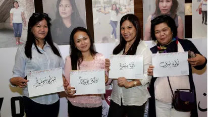 Four women holding signs in Arabic for Domestic Workers' Day celebration in Doha, Qatar