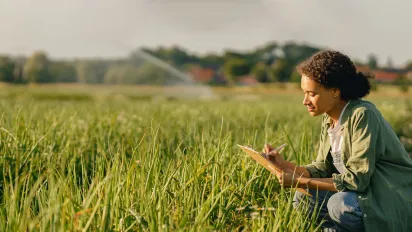 Female farmer writing on a clipboard while sitting in a field during harvest