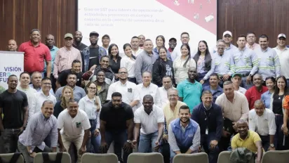Grupo grande de personas posando para una foto detrás se proyecta el letrero "Guía de SST para líderes de operación de actividades prioritarias en campo y cosecha en la cadena de suministro de la caña de azúcar" y a la izquierda se ve el pendón del Fondo Visión Cero