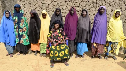 A group of women from Niger are standing in line behind their village leader seating in a chair